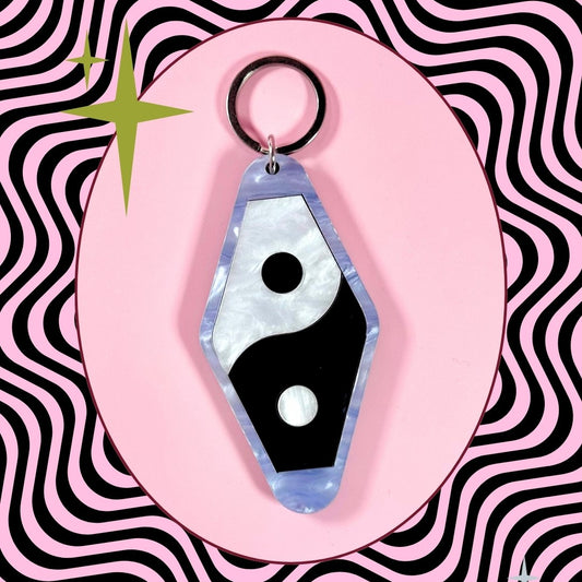 Keychain with a black and white design on a pink and black wavy pattern background