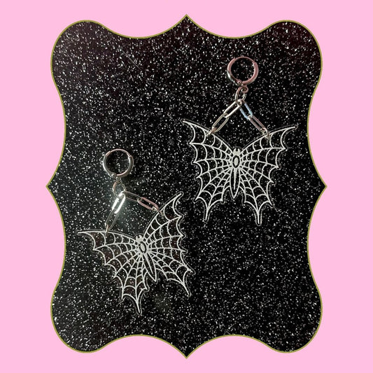 Spider web earrings on a black glittery card with pink background