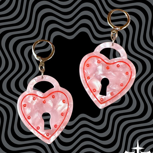 Heart-shaped lock keychains with pink glitter on a black and gray wavy background.