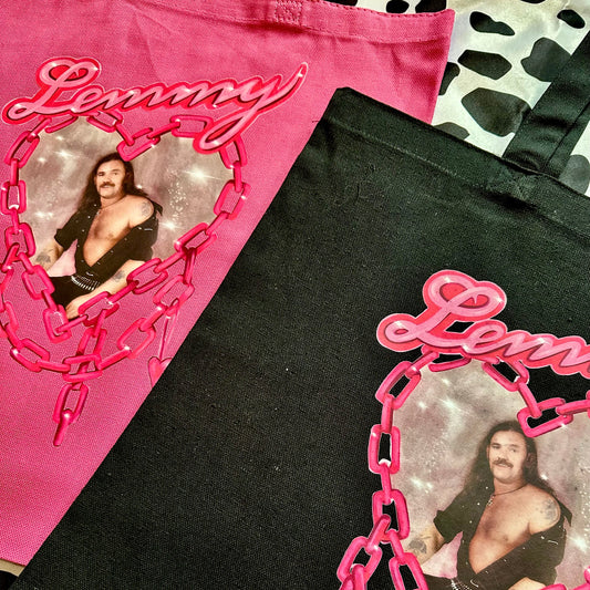Two tote bags shown in a flat-lay arrangement: one bright pink bag and one black bag, both featuring a large pink graphic with the word "Lemmy" in script, a heart-shaped chain design, and a printed photo of Lemmy Knight.