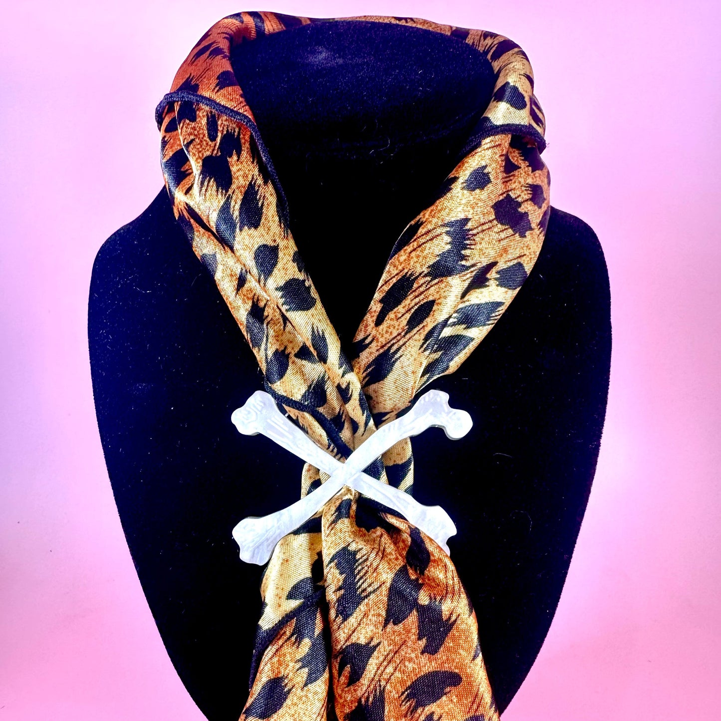 Leopard print scarf with bone-shaped clips on a black mannequin against a pink background