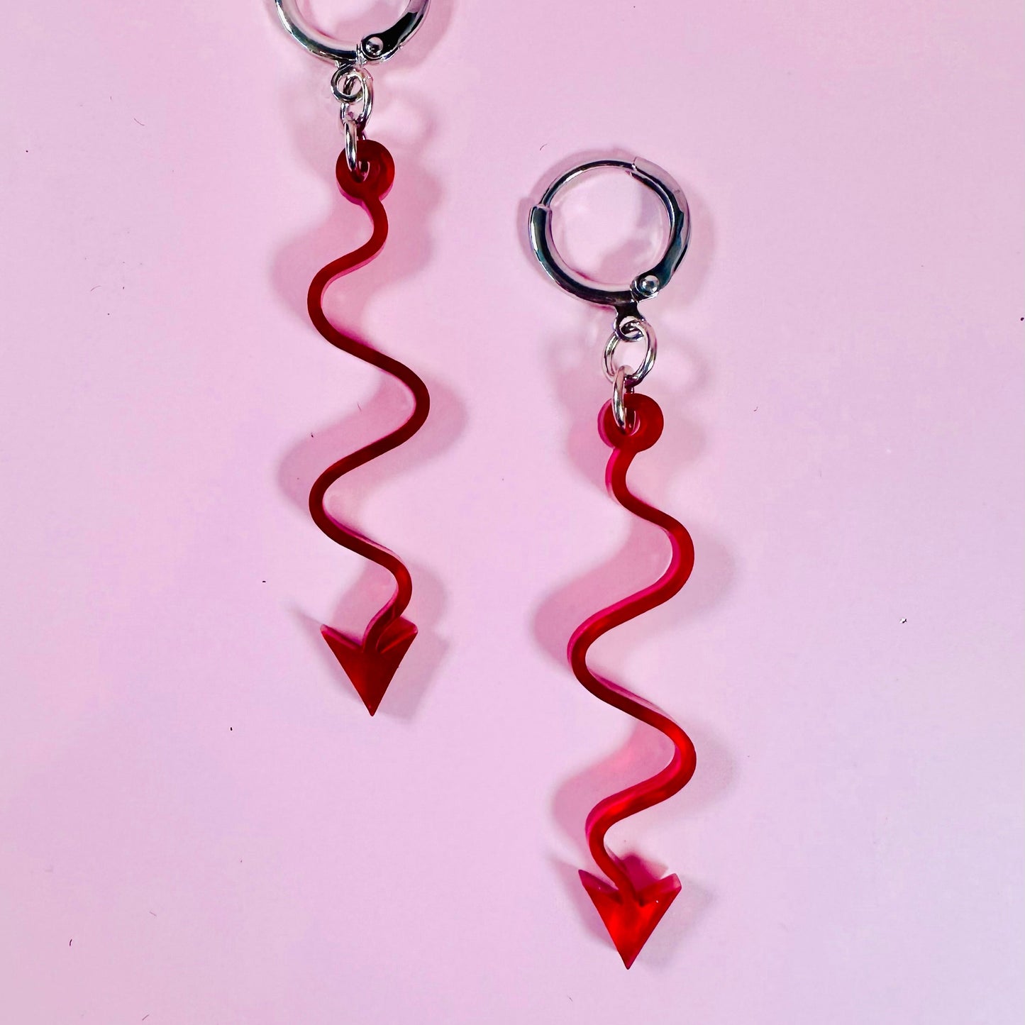 Red arrow-shaped earrings on a pink background