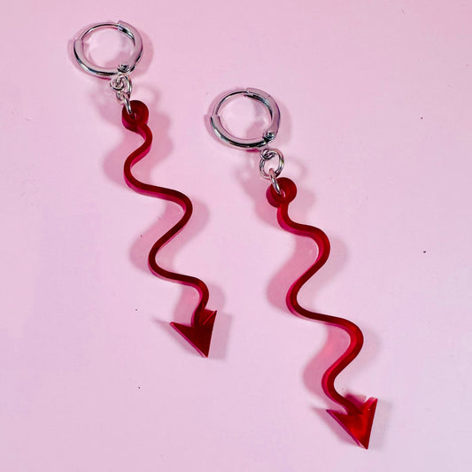 Red arrow-shaped earrings on a pink background