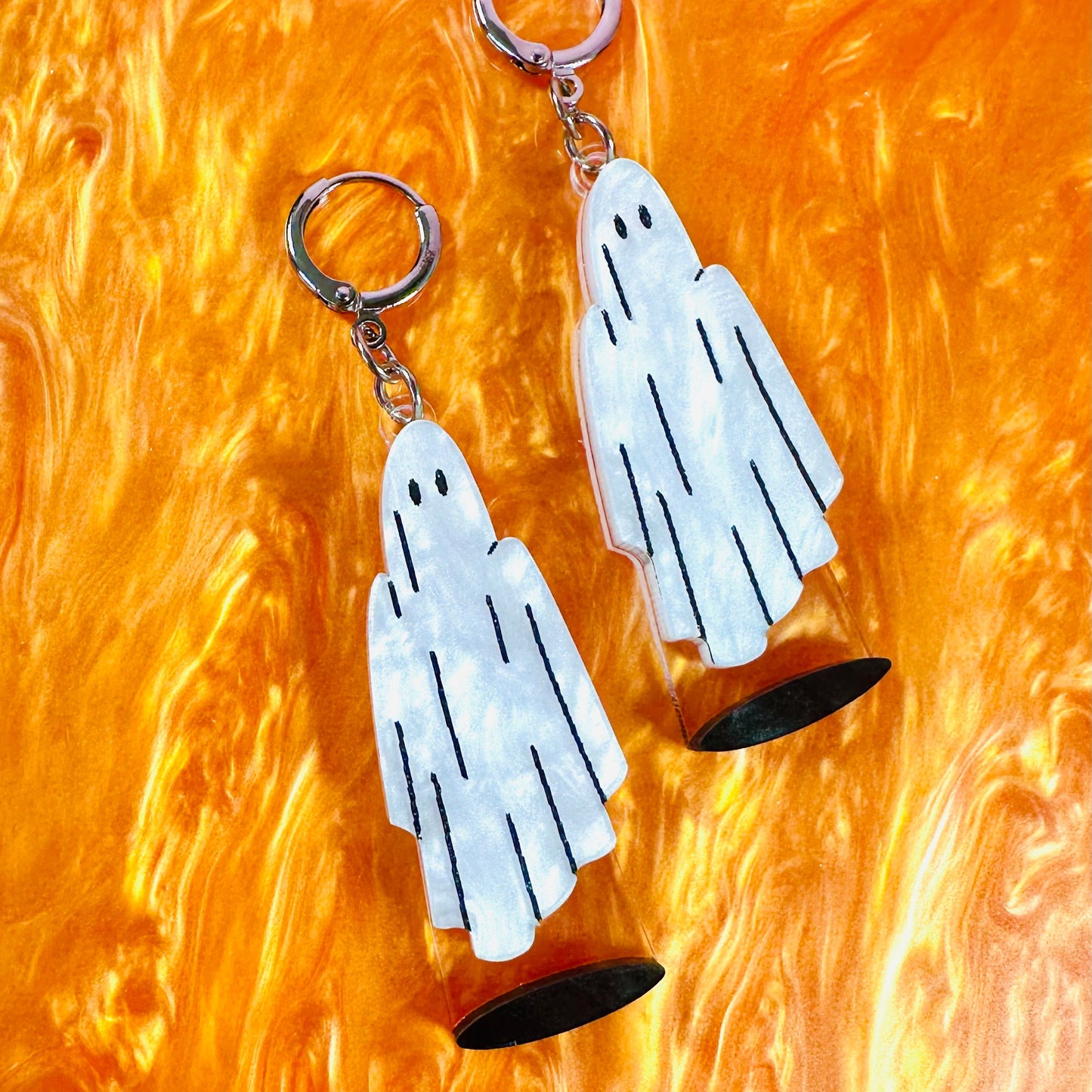 Ghost-shaped earrings on a textured orange background