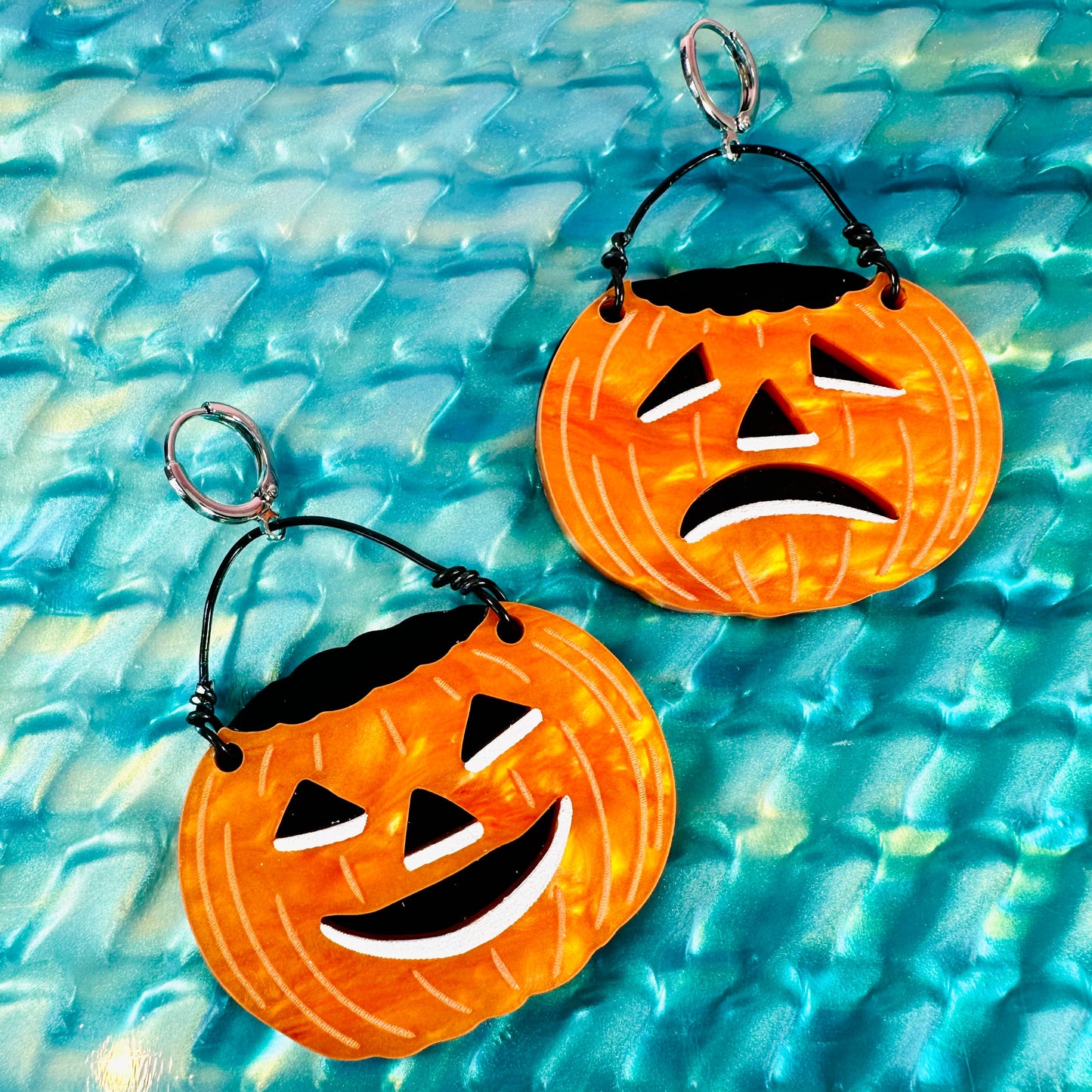 Halloween-themed pumpkin bucket earrings on a textured blue surface