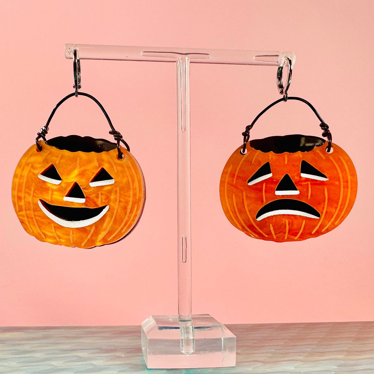 Halloween-themed earrings on a clear stand with a pink background