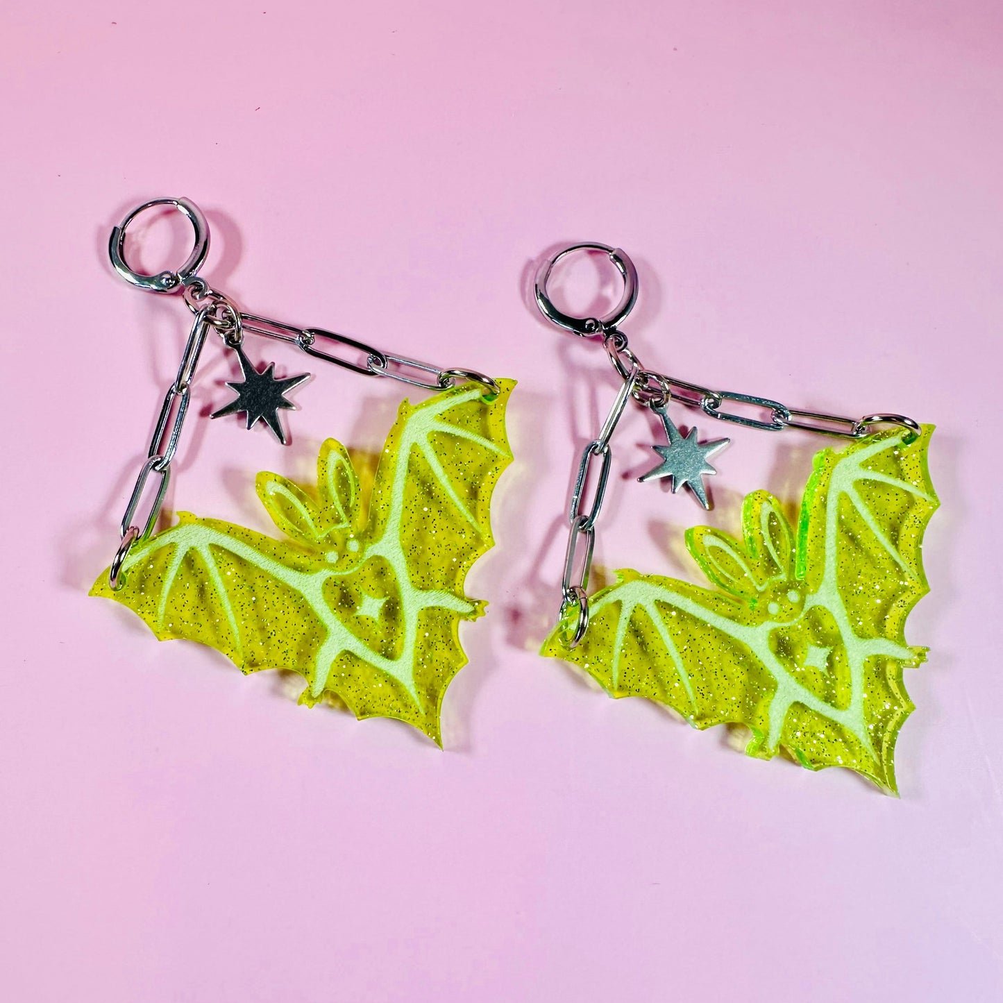 Pair of green bat-shaped earrings on a pink background