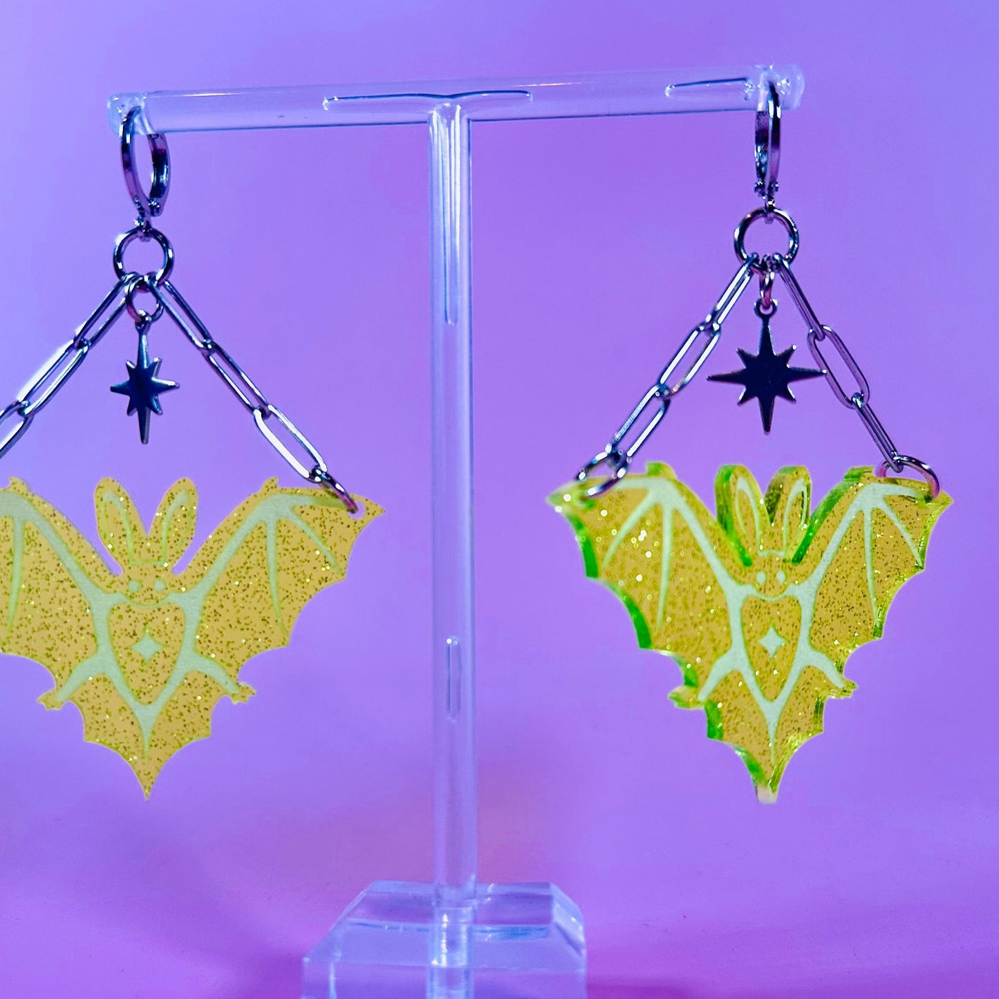 Bat-shaped earrings on a clear stand against a purple background
