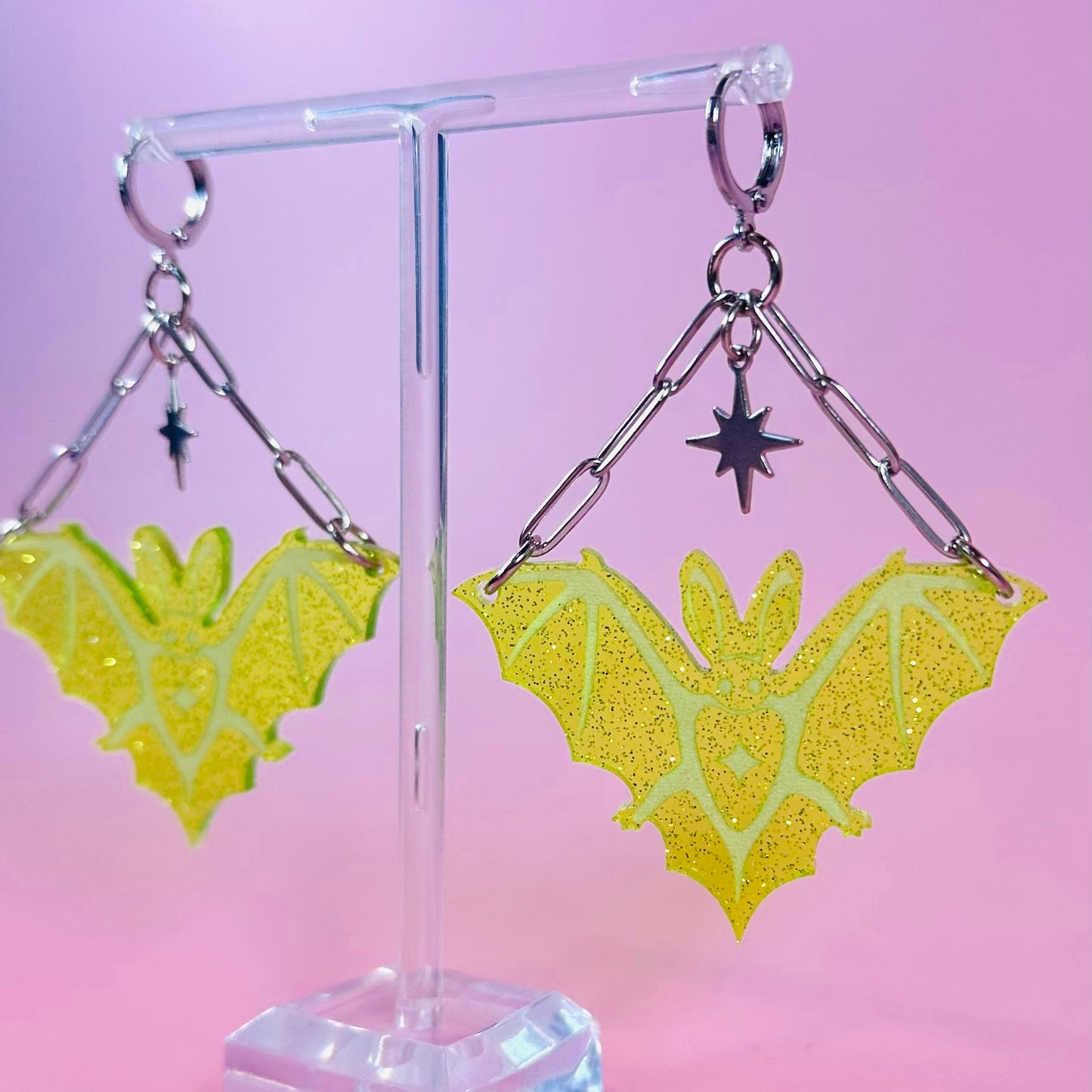 Yellow butterfly-shaped earrings on a clear stand against a pink background