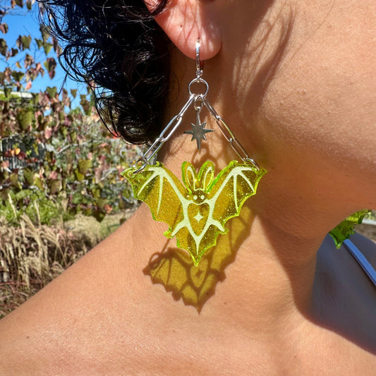 Close-up of a person wearing a green bat-shaped earring outdoors.
