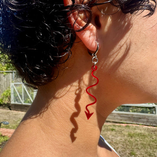 Close-up of a person wearing a red spiral earring outdoors.