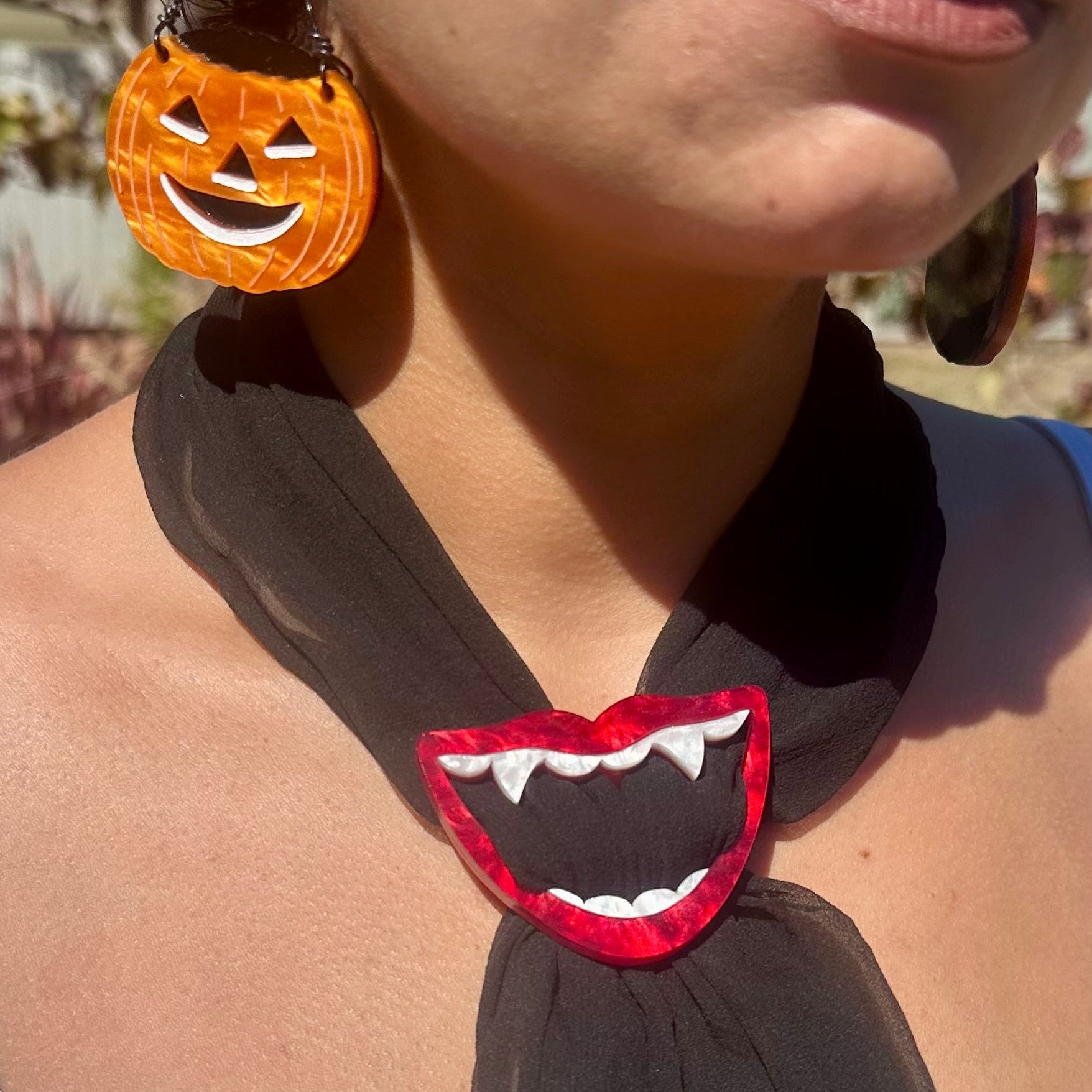 Person wearing a black scarf with a red mouth design and Halloween-themed earrings.