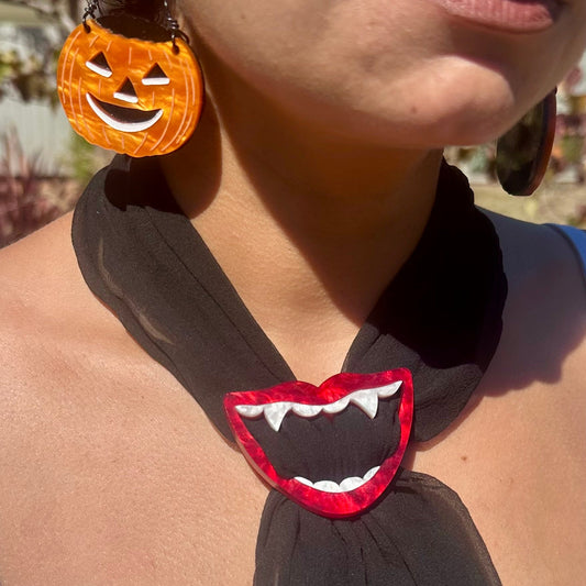 Person wearing a black scarf with a red mouth design and Halloween-themed earrings.