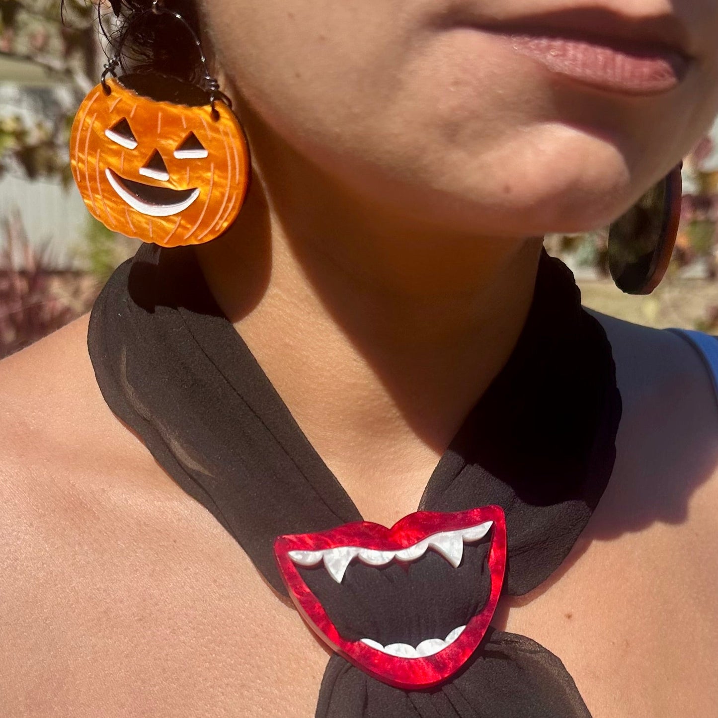 Person wearing a black scarf with a red mouth design and Halloween-themed earrings.