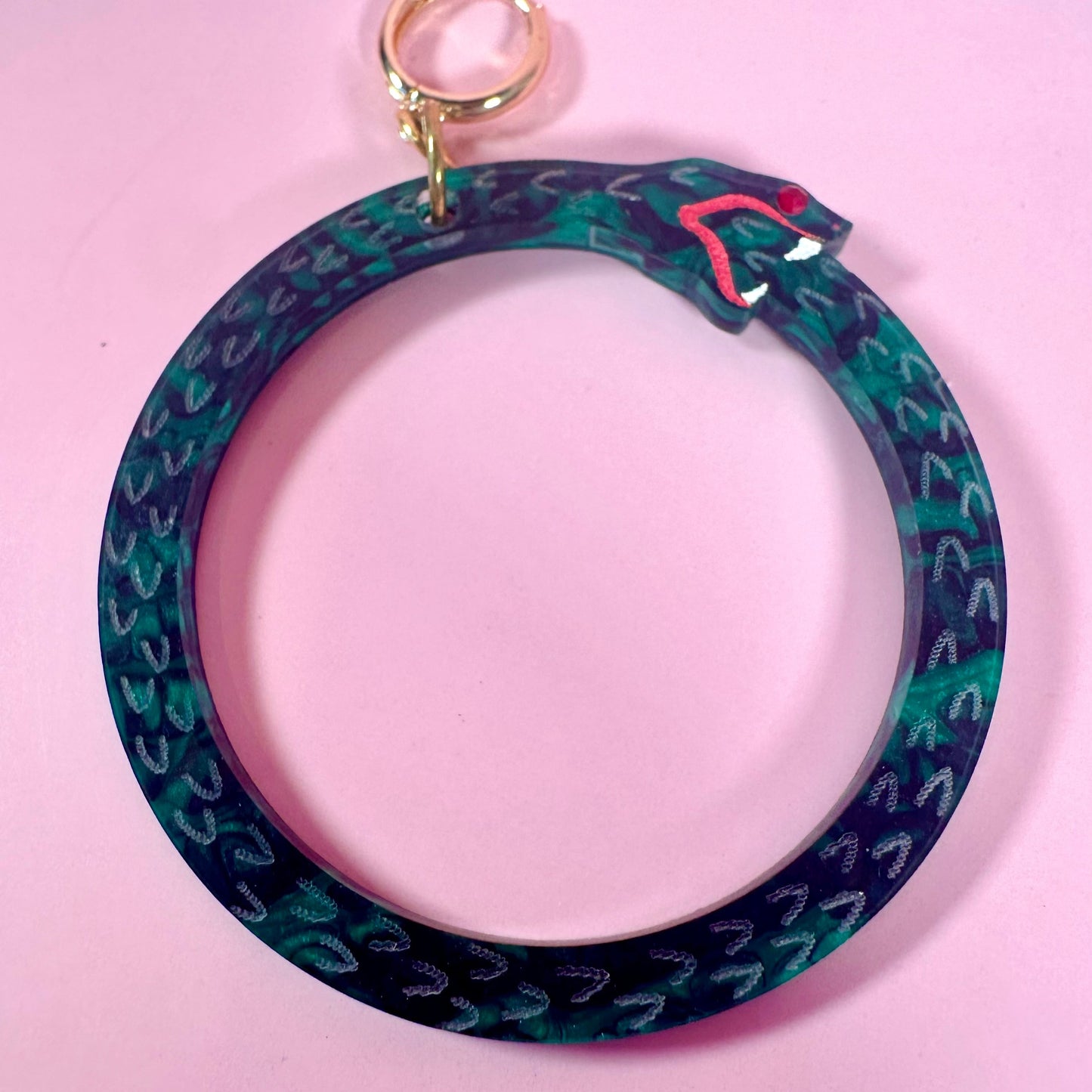 Circular keychain with blue and green pattern on a pink background