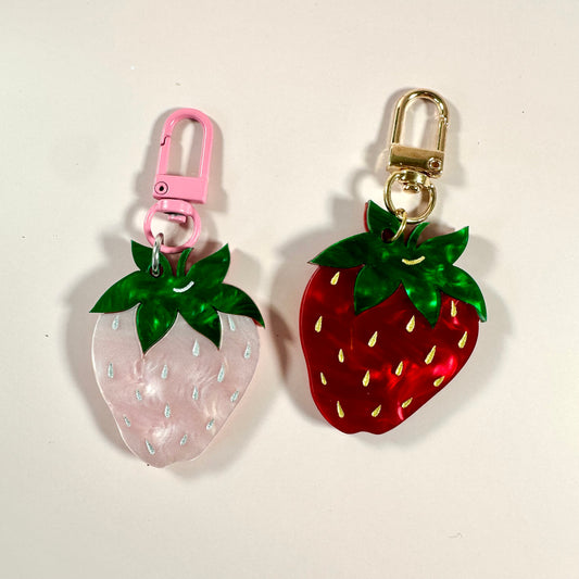 Two strawberry-shaped keychains, one pink and one red, on a light background.