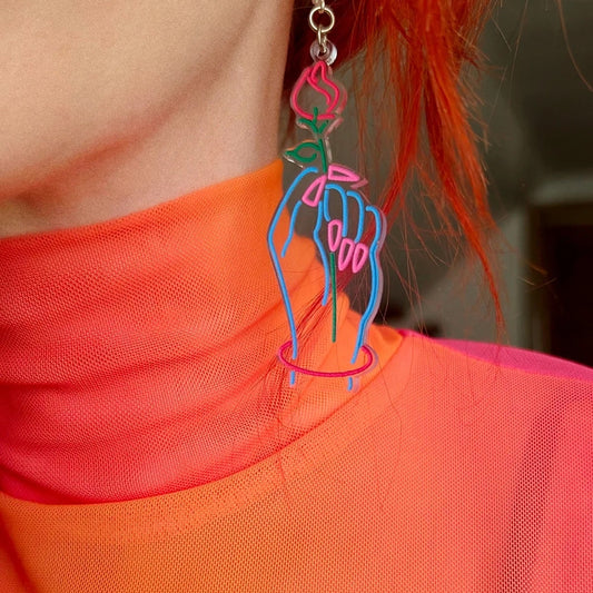Person wearing a unique earring with a colorful design on an orange shirt.
