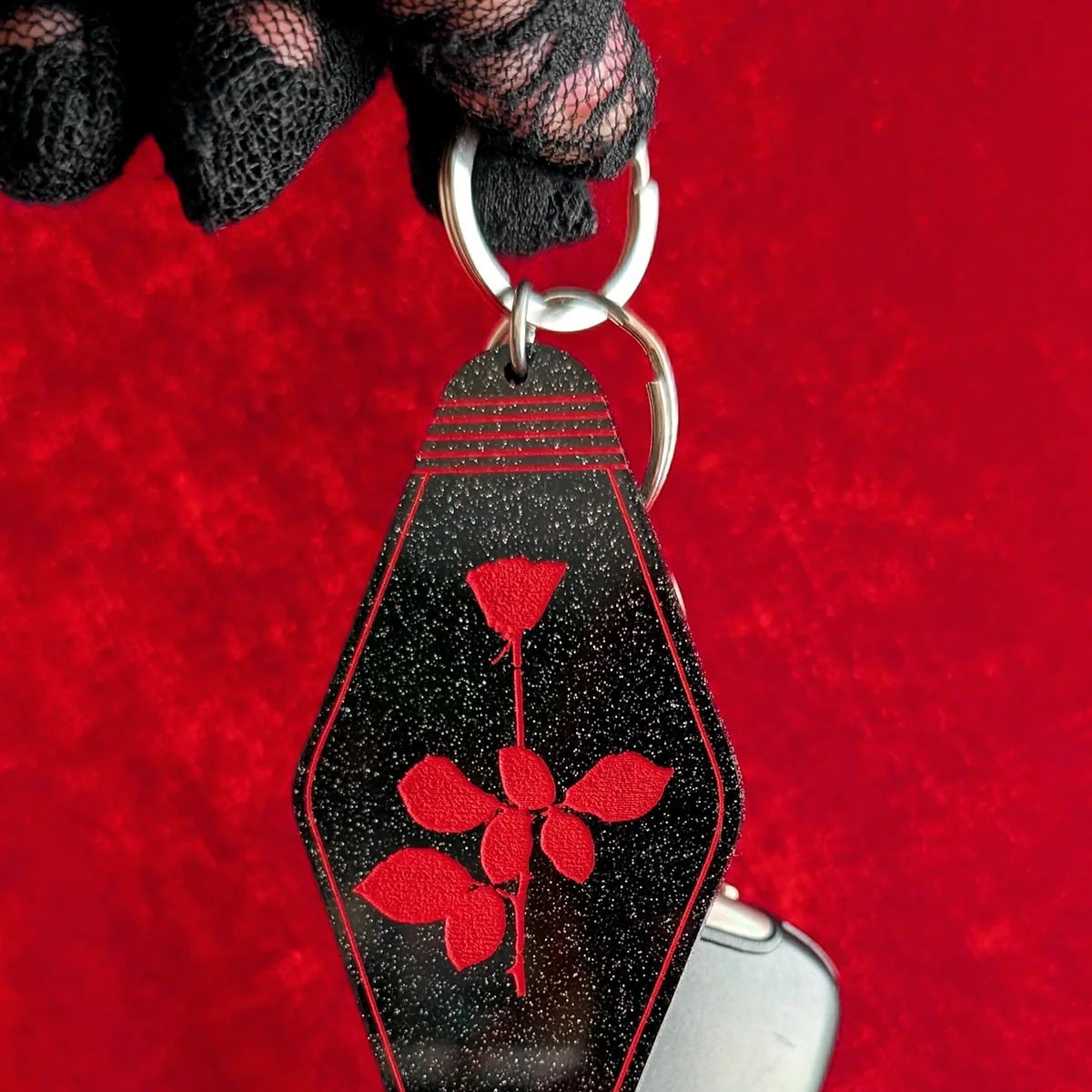 Keychain with red floral design on a black background attached to a car key on a red surface