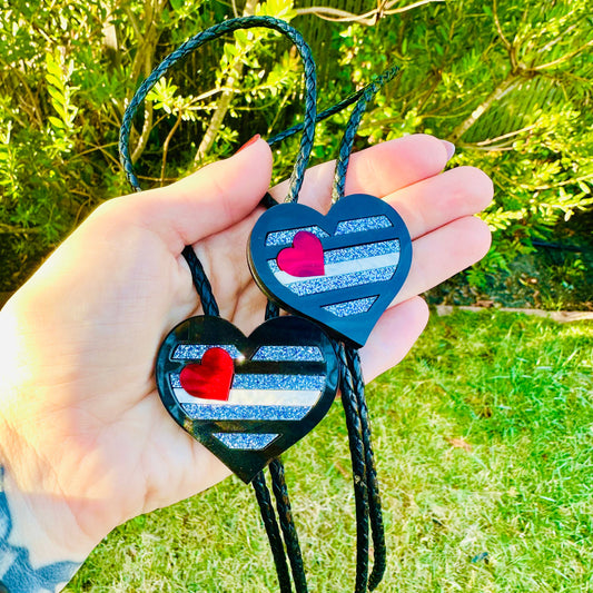 Heart-shaped keychains with striped patterns held by a hand against a green outdoor background