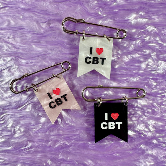 Three safety pin brooches with 'I ❤️ CBT' text on a purple textured background