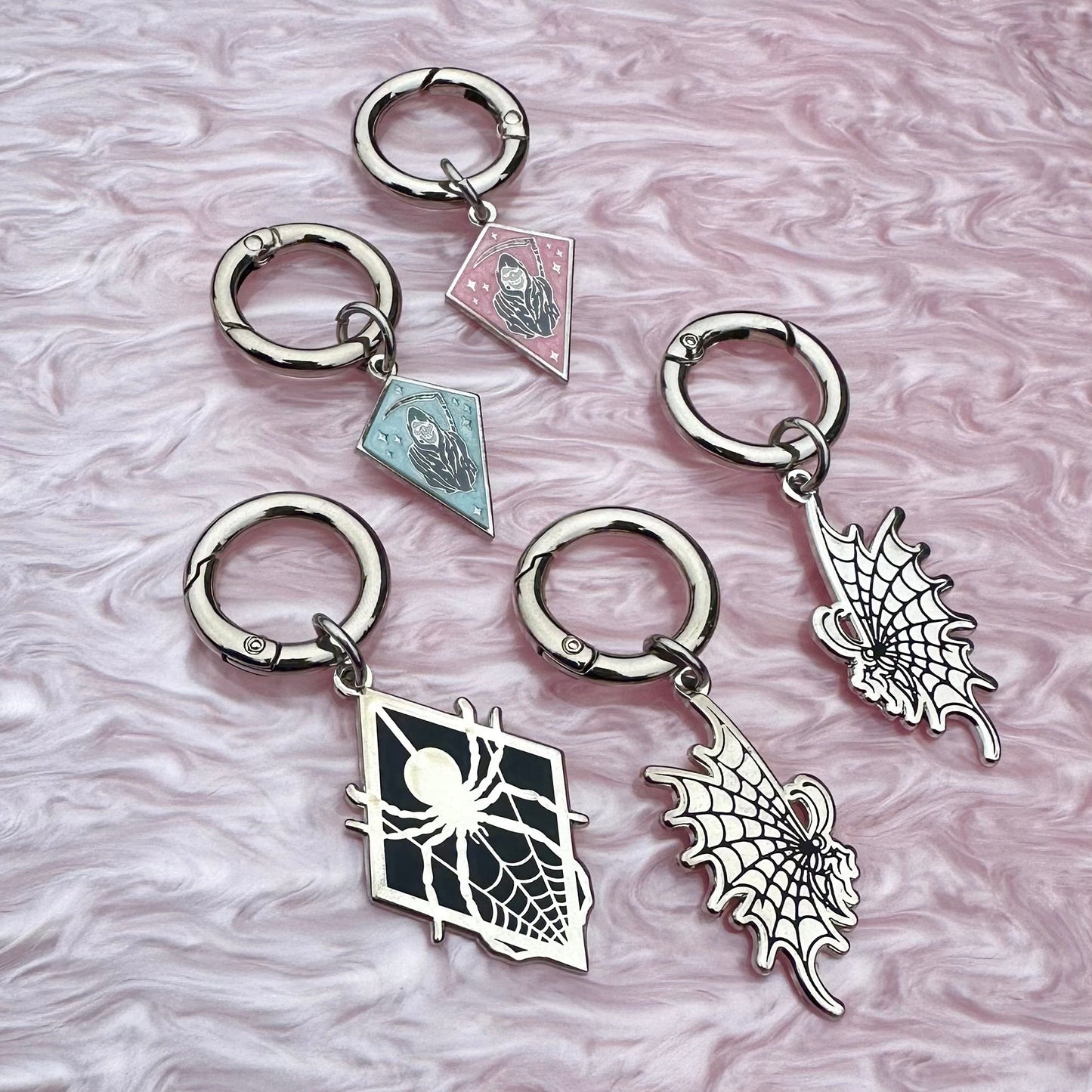 Set of spider-themed keychains on a marbled pink and gray background