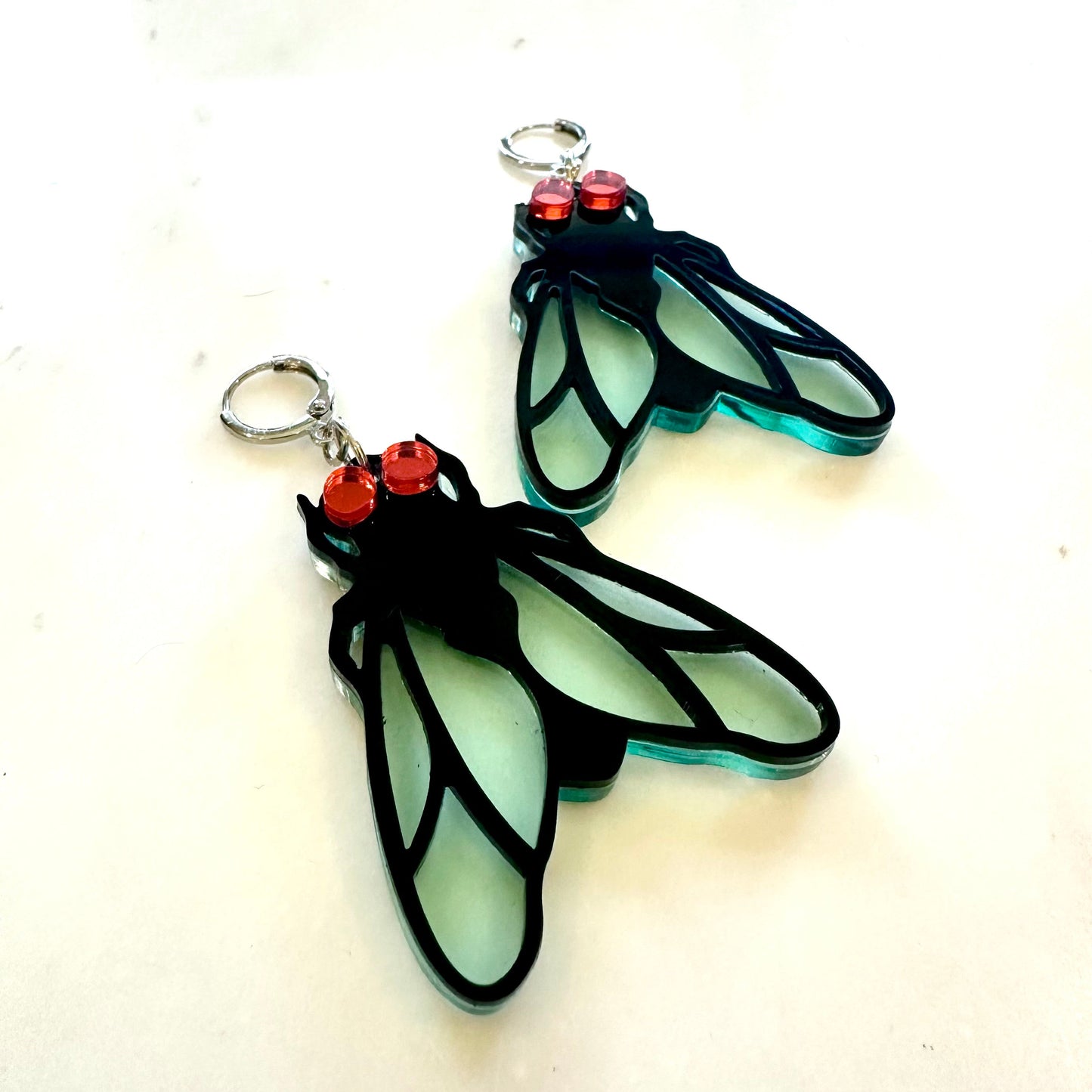 Insect-shaped earrings with red accents on a white background