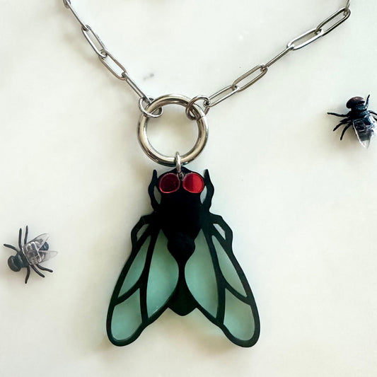 Pendant shaped like a fly with red eyes on a chain, surrounded by small black flies on a white background