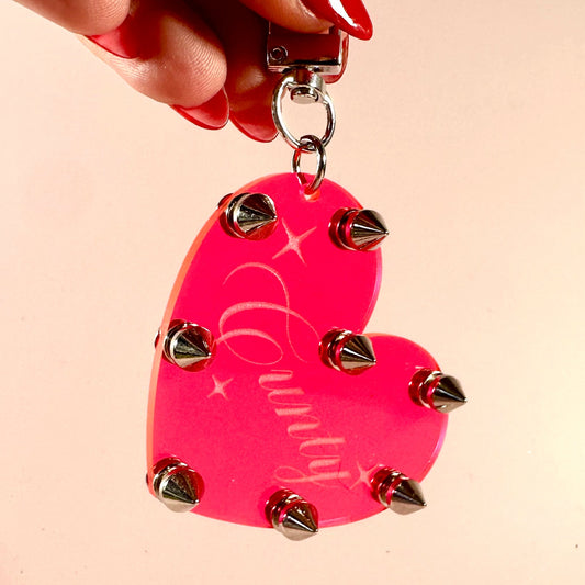 Pink heart-shaped keychain with studs held by a hand on a beige background