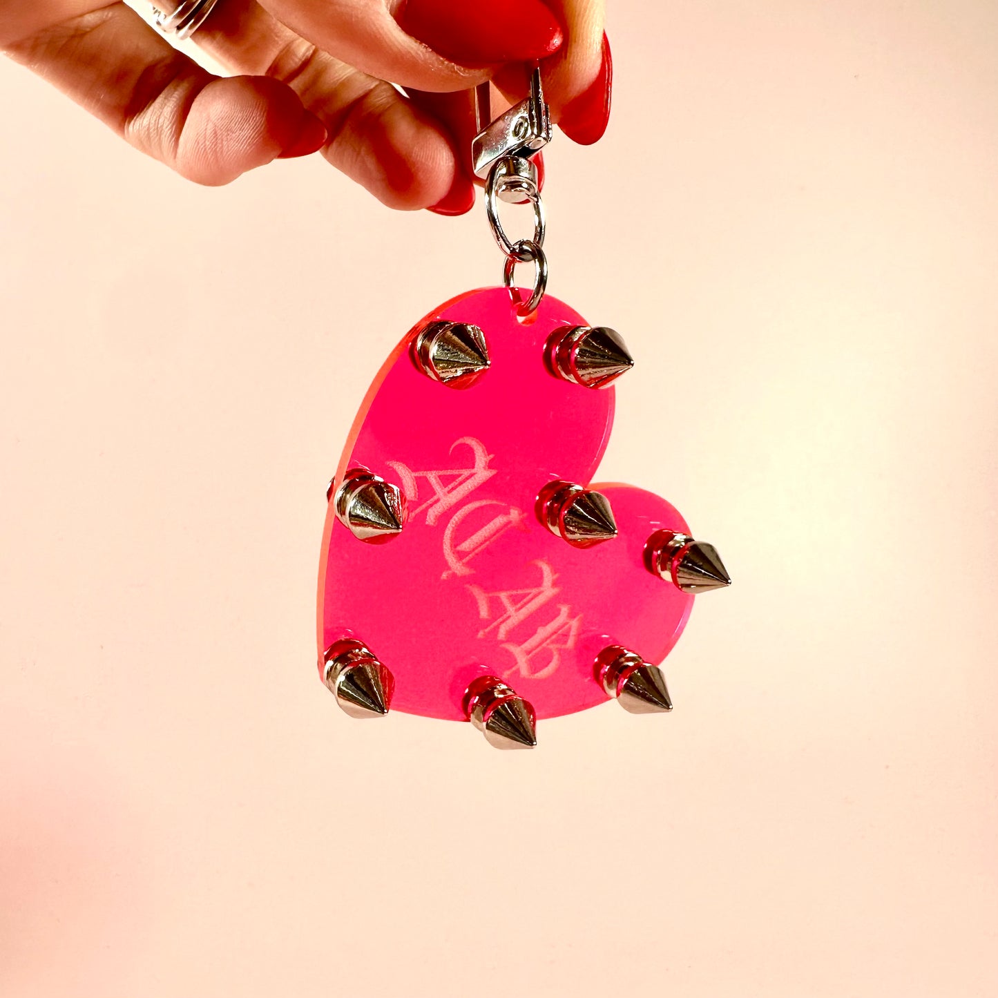Pink heart-shaped keychain with silver spikes held by a hand against a beige background
