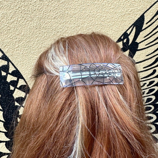 Person with a decorative hair clip in their hair against a patterned wall.