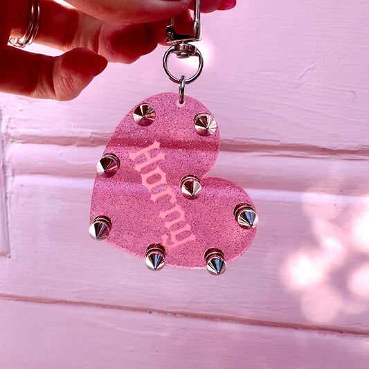 Pink heart-shaped keychain with studs held by a hand against a light pink background