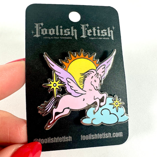Pin with a unicorn design on a Foolish Fetish card held by a hand with red nail polish.