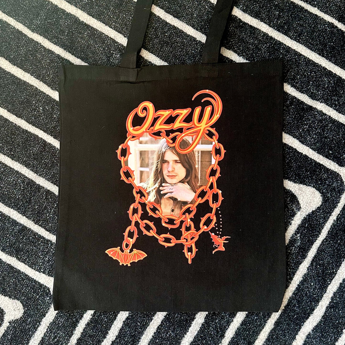 Black tote bag with 'Ozzy' design on a striped background