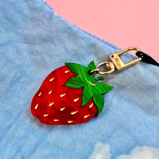 Strawberry-shaped keychain attached to a blue bag with a pink background