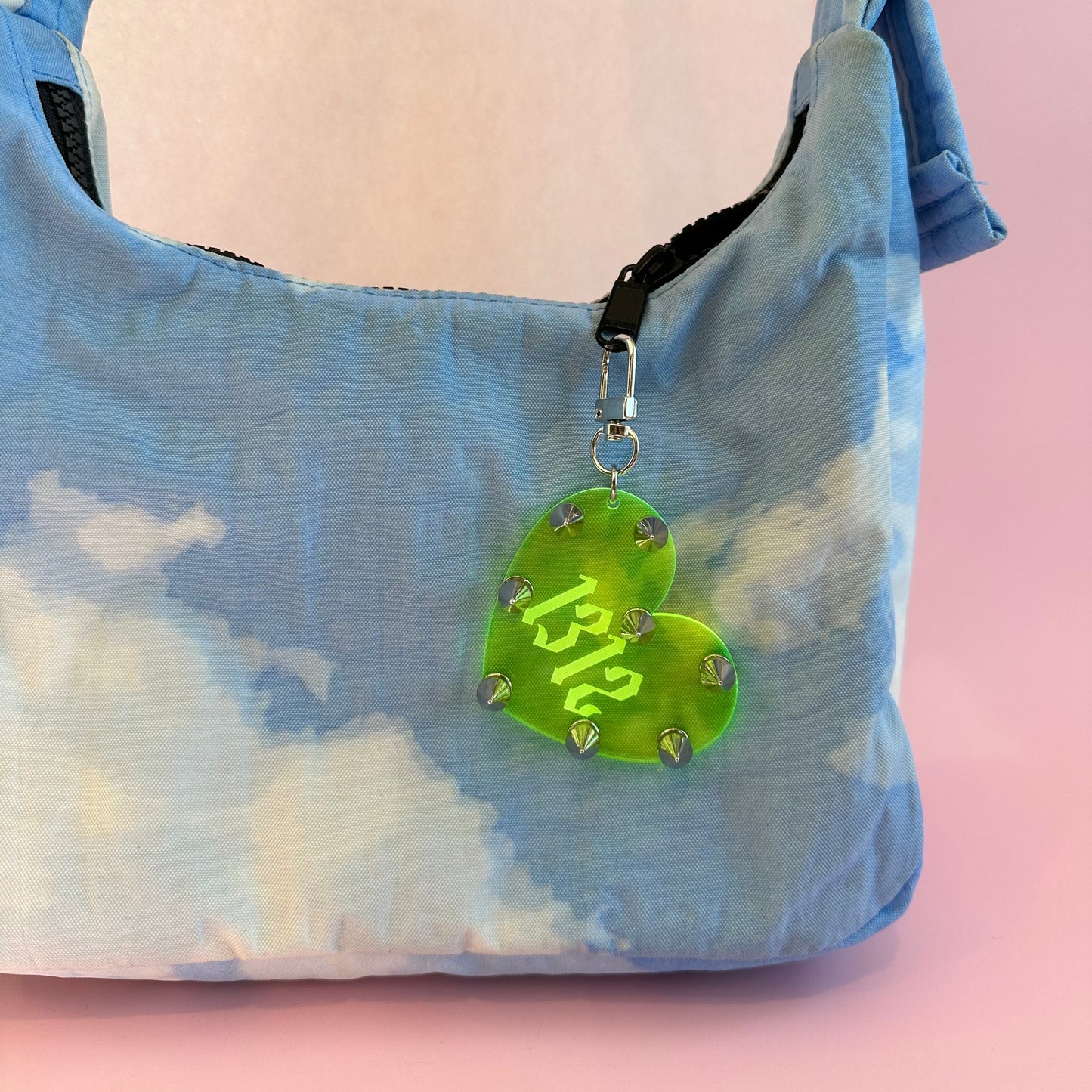 Heart-shaped green tag with '1312' on a blue tie-dye bag against a pink background