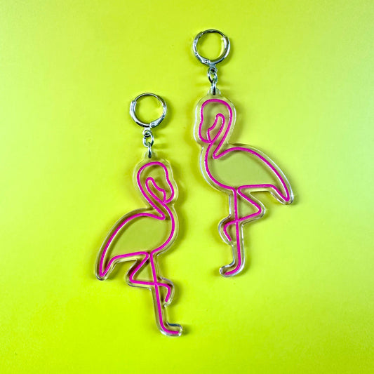 Two pink flamingo-shaped earrings with silver metal rings, displayed on a bright yellow-green background.