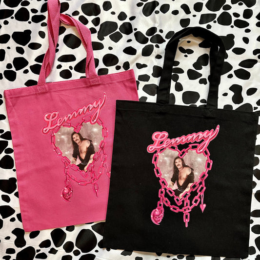Two custom canvas tote bags, one pink and one black, displayed on a black and white cow print background. Each bag features a custom heart-shaped photo print and the name 'Lemmy' in pink script.