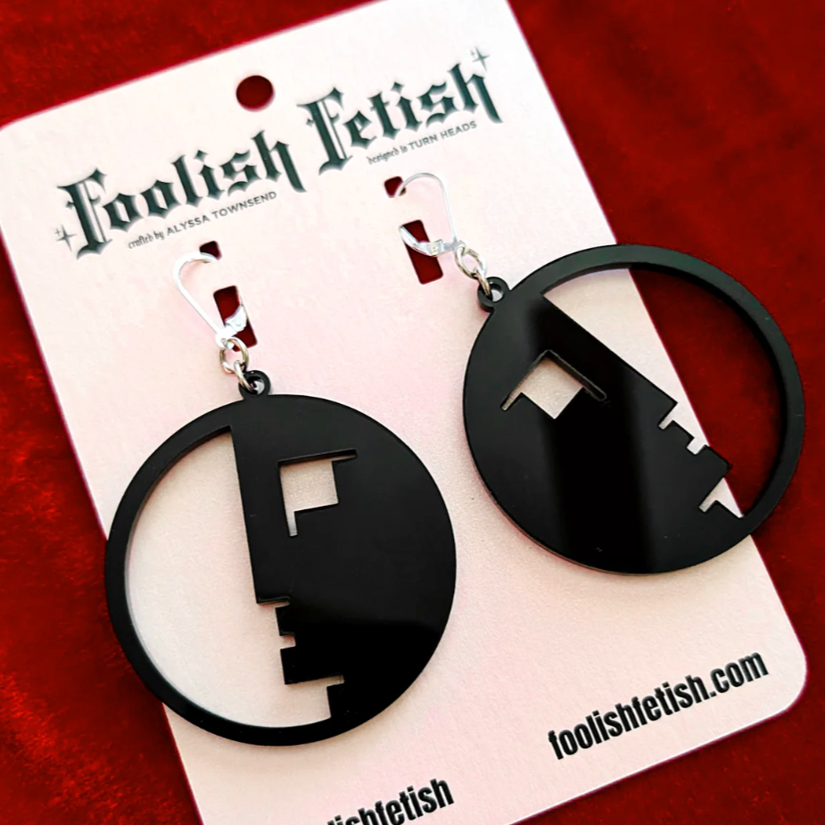 Black earrings on a 'Foolish Fetish' branded card against a red background