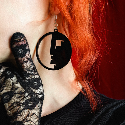 Black circular earring with cut-out design worn by a person with red hair.