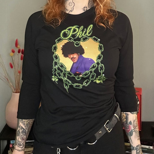 Person wearing a black t-shirt with a graphic design, standing in a room with a gray wall and colorful decor.