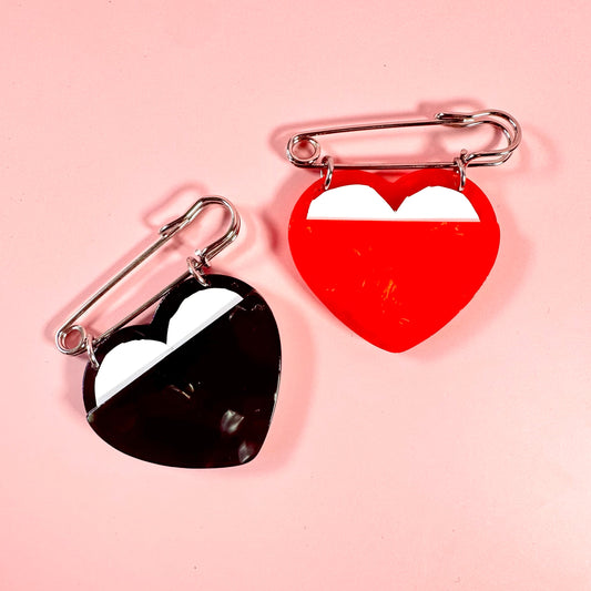 Two heart-shaped pins, one black and one red, on a pink background.