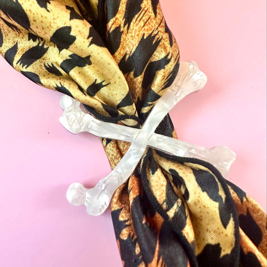 white crossbones scarf ring on leopard print scarf on pink background