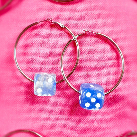 Hoop earrings with blue dice-shaped charms on a pink fabric background