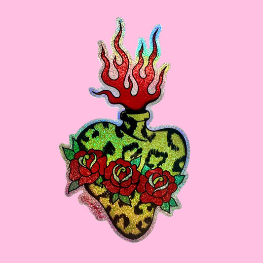 A decorative heart-shaped patch with a leopard print pattern, red roses, and red flames on top, shown on a solid pink background.