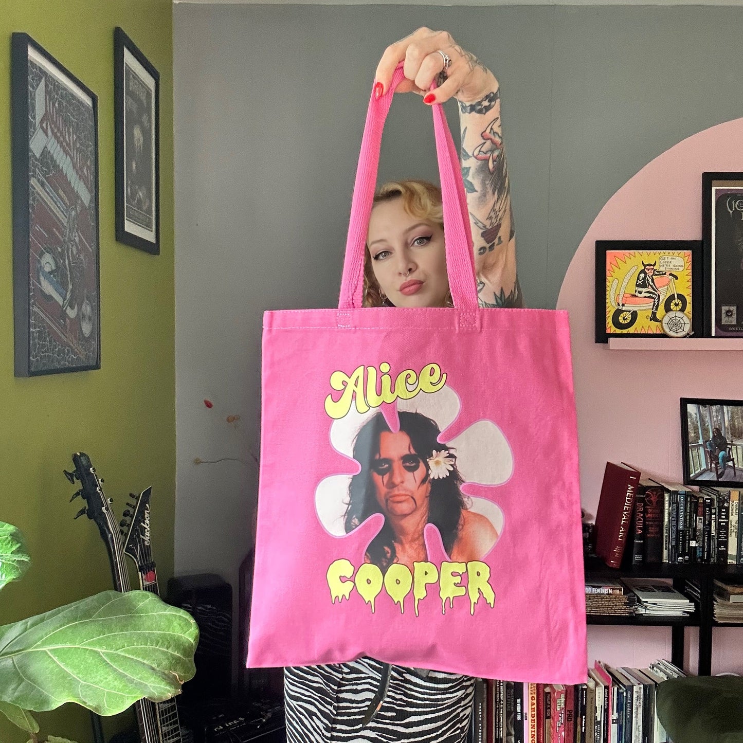 Person holding a pink tote bag with 'Alice Cooper' design in a room.