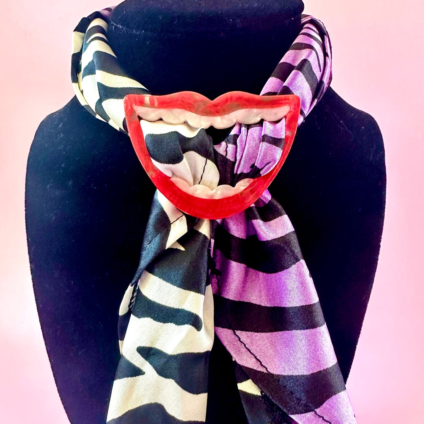 A scarf with a split design, featuring a black and cream zebra print on one side and purple and black stripes on the other, styled on a black mannequin bust against a pink background.