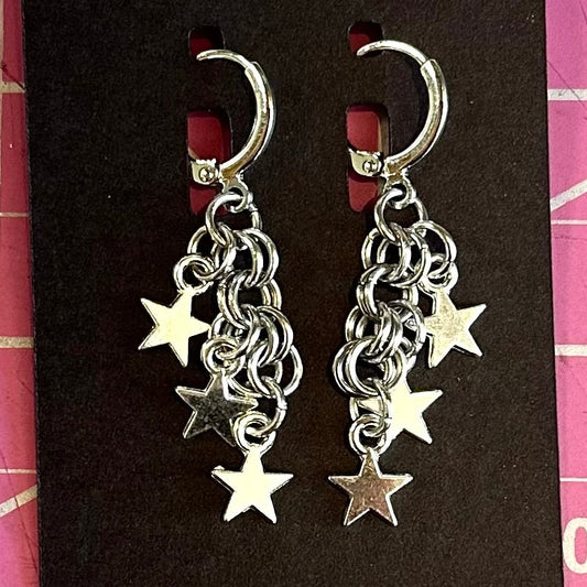 Pair of silver star earrings on a Foolish Fetish branded card against a pink grid background.