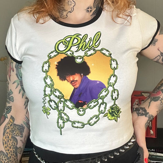 Person wearing a white t-shirt with a graphic design of a person in a purple outfit and text 'Phil'.