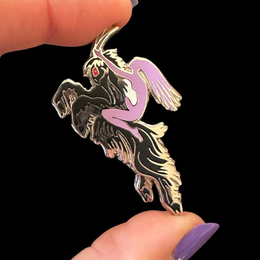 Gold and purple dragon-shaped pendant held between fingers against a black background