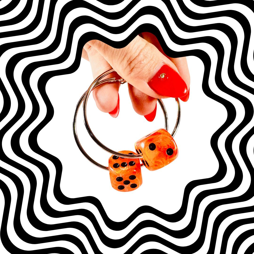 Hand holding a keychain with dice-shaped charms against a black and white wavy pattern